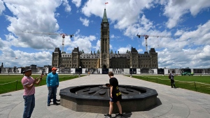 Visitors to Parliament Hill take in the Centennial Flame in front of Centre Block’s Peace Tower, in Ottawa, on Friday, June 17, 2022. THE CANADIAN PRESS/Justin Tang