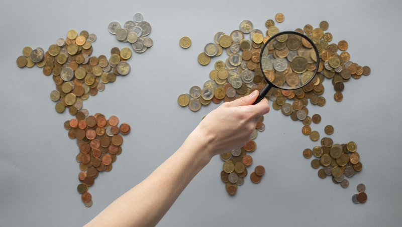 Anonymous person magnifying view of coins shaped in world map.  (Pexels/Monstera)
