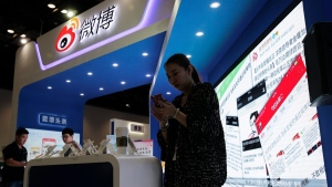 In this April 28, 2016, file photo, a woman browses her smartphone near a display booth for China's Weibo microblogging website at the 2016 Global Mobile Internet Conference in Beijing. (AP Photo/Andy Wong, File)