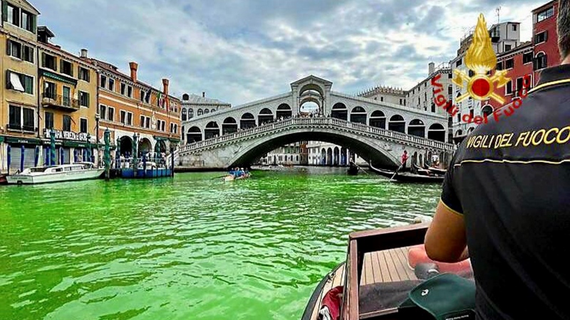 In this image released by the Italian firefighters, a firefighter on a boat looks at the arched Rialto Bridge along Venice's historical Grand Canal as a patch of phosphorescent green liquid spreads in it, Sunday, May 28, 2023. (Vigili Del Fuoco via AP)
