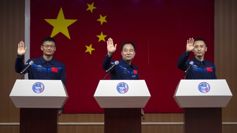 Chinese astronauts for the upcoming Shenzhou-16 mission, from left, Gui Haichao, Jing Haipeng, and Zhu Yangzhu wave as they stand behind glass during a meeting with the press at the Jiuquan Satellite Launch Center in northwest China on Monday, May 29, 2023. (AP Photo/Mark Schiefelbein)