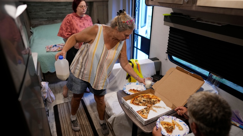 Jacquelyn, center, and Timothy Velazquez share a pizza inside the small camper where they are living with their daughter Hannah, top, home from college and working for the summer, while they wait to be able repair their home, which was damaged when Hurricane Ian's storm surge rose to within inches of their ceiling, in Fort Myers Beach, Fla., Wednesday, May 24, 2023. (AP Photo/Rebecca Blackwell)