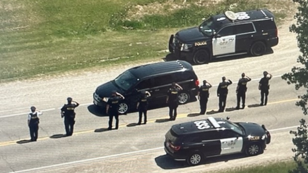 OPP officers salute as the body of Det. Const. Steven Tourangeau is removed from the scene of a crash in Oxford County on May 29, 2023. (CTV News)