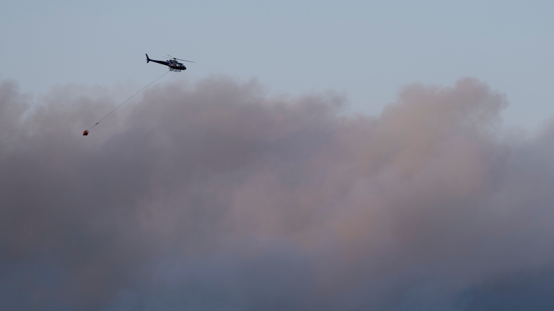 A helicopter carrying water flies through heavy smoke as an out-of-control wildfire in a suburban community outside of Halifax quickly spread, engulfing multiple homes and forcing the evacuation of local residents on Sunday May 28, 2023. (THE CANADIAN PRESS/Darren Calabrese)