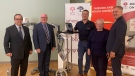 Environment and Climate Change Minister Gary Grossman, Health Minister Bruce Fitch, medical radiation technologist Todd Gordon, Social Development Minister Dorothy Shephard, and Minister responsible for La Francophonie Glen Savoie pose with one of seven portable X-ray machines in Saint John on May 29, 2023. (CTV Atlantic/Avery MacRae)