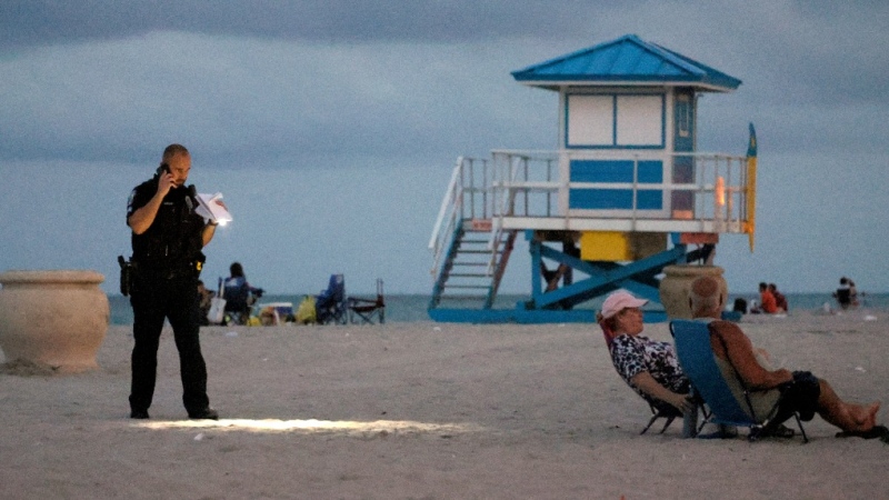 A police officer shines his flashlight downward as he pauses on Hollywood Beach while investigating a shooting Monday, May 29, 2023, in Hollywood, Fla. Multiple people were injured Monday evening when gunfire erupted along the beach boardwalk. (Mike Stocker/South Florida Sun-Sentinel via AP)