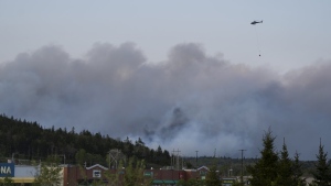 A helicopter carrying water flies over heavy smoke from an out-of-control fire in a suburban community outside of Halifax that spread quickly, engulfing multiple homes and forcing the evacuation of local residents on Sunday May 28, 2023. (THE CANADIAN PRESS/Darren Calabrese)