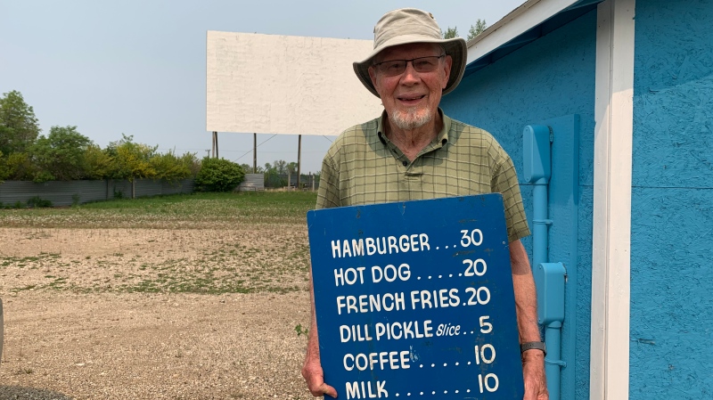 Burt Crawford holds an original concession sign, which displays the price of a hamburger at 30 cents, a hot dog for 20 cents and coffee or hot chocolate for 10 cents. (Carla Shynkaruk / CTV News)