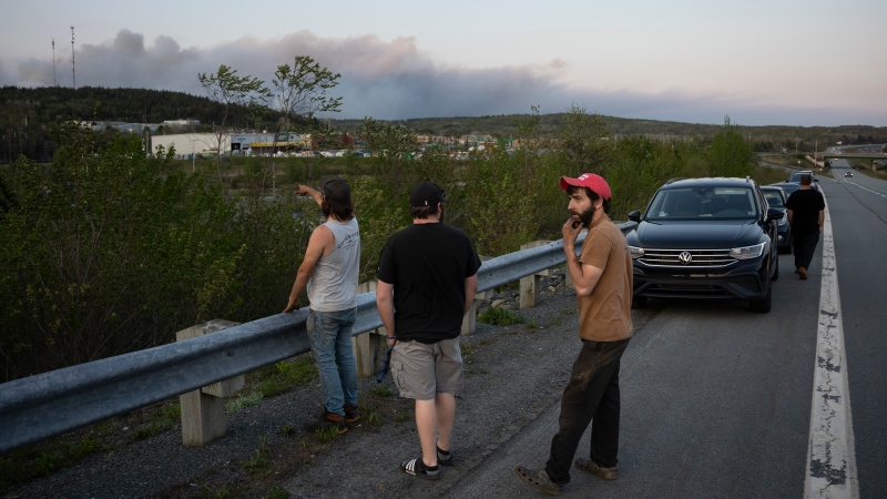 People stop on the side of the road where police set up a roadblock as heavy smoke fills the sky from an out-of-control in a suburban community outside of Halifax quickly spread, engulfing multiple homes and forcing the evacuation of local residents on Sunday May 28, 2023.THE CANADIAN PRESS/Darren Calabrese