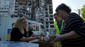 Local residents get free meals from volunteers against the background of their apartment house, damaged in the Russian rocket attack, in Kharkiv, Ukraine, Friday, June 2, 2023. (AP Photo/Andrii Marienko)