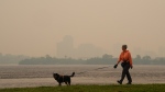 A woman walks her dog along the Ottawa River in Ottawa as smoke from wildfires obscures Gatineau, Que., in the distance on June 6, 2023. (THE CANADIAN PRESS/Sean Kilpatrick)