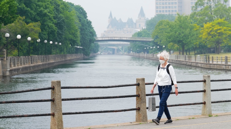 A person wears a mask as they walk along the Rideau Canal in Ottawa on Wednesday, June 7, 2023. Forest fire smoke continue to shroud the Nations Capital and triggering air quality advisoryies. (Sean Kilpatrick/THE CANADIAN PRESS)