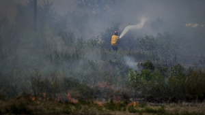 A firefighter directs water on a grass fire on an acreage behind a residential property in Kamloops, British Columbia, Monday, June 5, 2023. For the first time this year, air quality advisories are posted for part of Vancouver Island and a large section of the Lower Mainland as smoke from several wildfires wafts over the region. THE CANADIAN PRESS/Darryl Dyck