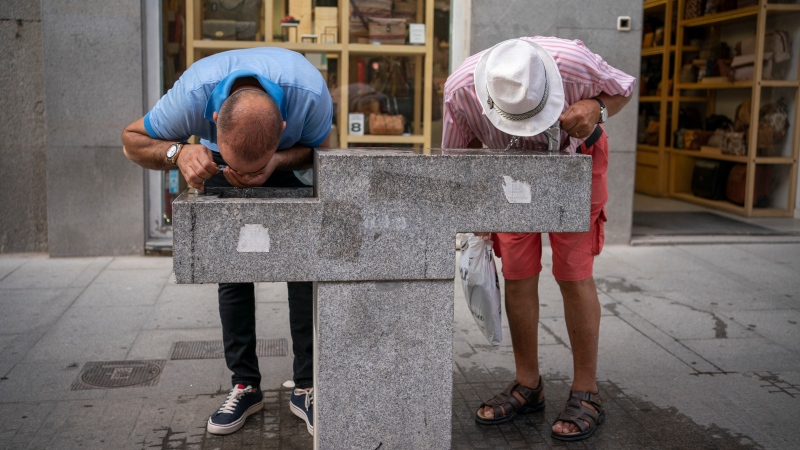 Two men drink water from a fountain in during a heatwave in Madrid, Spain on Aug. 14, 2021. (AP Photo/Andrea Comas)