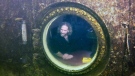 In this photo provided by the Florida Keys News Bureau, diving explorer and medical researcher Dr. Joseph Dituri peers out of a large porthole, Saturday, May 13, 2023, at Jules' Undersea Lodge positioned at the bottom of a 30-foot-deep lagoon in Key Largo, Fla. On Saturday, Dituri broke a record for the longest time living underwater at ambient pressure, his 74th day of a planned 100-day mission living submerged in the Florida Keys. The previous underwater habitation record of 73 days, two hours and 34 minutes was set by two professors from Tennessee in 2014 at the same location. Dituri's underwater mission, dubbed Project Neptune 100, was organized by the Marine Resources Development Foundation and combines medical and ocean research along with educational outreach. (Frazier Nivens/Florida Keys News Bureau via AP)
