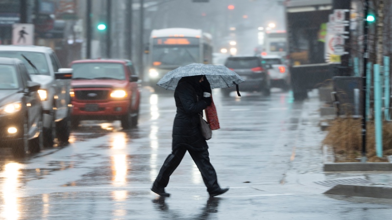 A pedestrian shields themselves from rain and wind during a rainfall warning in Halifax on Thursday, January 26, 2023. (Courtesy: THE CANADIAN PRESS/Darren Calabrese)