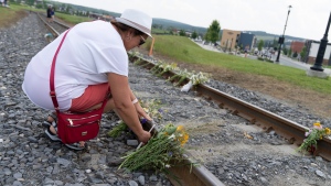 A woman leaves candles on the train tracks following a commemorative mass in memory of the 47 victims and their families on the tenth anniversary of the train derailment in Lac Megantic, Que. on Thursday, July 6, 2023. THE CANADIAN PRESS/Christinne Muschi