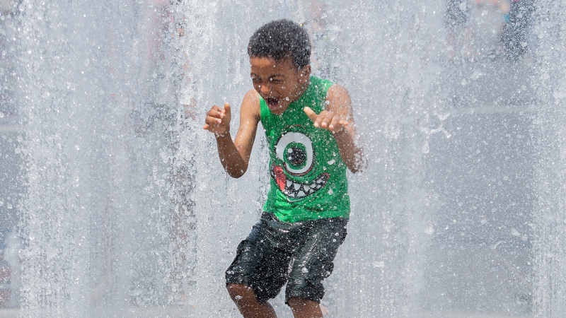 FILE: David Adejor (6) beats the heat as he runs through water fountains in Montreal. THE CANADIAN PRESS/Graham Hughes
