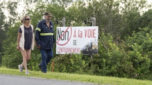 Rita Boulanger and Raymond Savoie walk past a sign stating "No to the bypass" on their property in Lac-Mégantic, Que., on Thursday, July 6, 2023. The couple faces losing their home as the federal government plans to expropriate land from some residents in Lac-Megantic and surrounding towns to build a rail bypass to remove trains from the town's downtown area. THE CANADIAN PRESS/Christinne Muschi