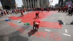 Family and supporters paint a red dress as they gather to protest all levels of governments' lack of action in funding a search of Winnipeg's landfills for missing women at Portage and Main in Winnipeg, Thursday, August 3, 2023. THE CANADIAN PRESS/John Woods