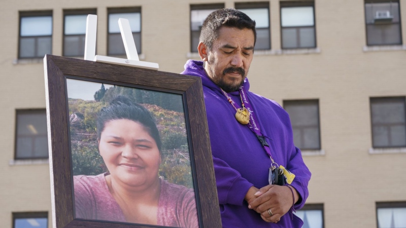 Carol Dubé, husband of Joyce Echaquan, stands next to a photo of his deceaced wife in front of the hospital where she died, in Joliette, Que., during a memorial on Sept. 28, 2021, marking the first anniversary of the death of his wife. THE CANADIAN PRESS/Paul Chiasson
