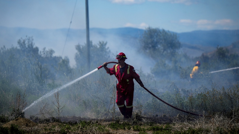 A firefighter directs water on a grass fire burning on an acreage behind a residential property in Kamloops, British Columbia, on Monday, June 5, 2023. (Darryl Dyck/The Canadian Press via AP)