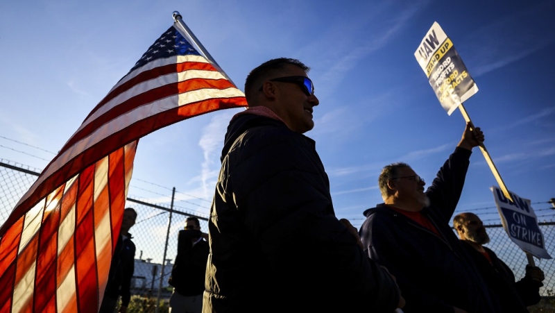 UAW members Dan Schlieman, with flag, and Brad Geer work the picket line during a strike Tuesday, Sept. 19, 2023, at the Stellantis Toledo Assembly Complex where Jeeps are made in Toledo, Ohio. (Jeremy Wadsworth/The Blade via AP)