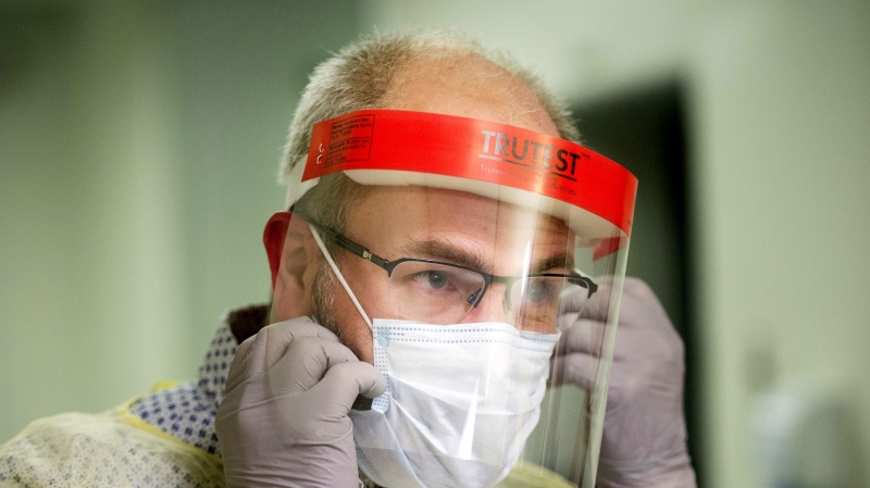 A man demonstrates how to put on a face mask and other protective clothing during a tour of a COVID-19 evaluation clinic in Montreal, Tuesday, March 10, 2020.