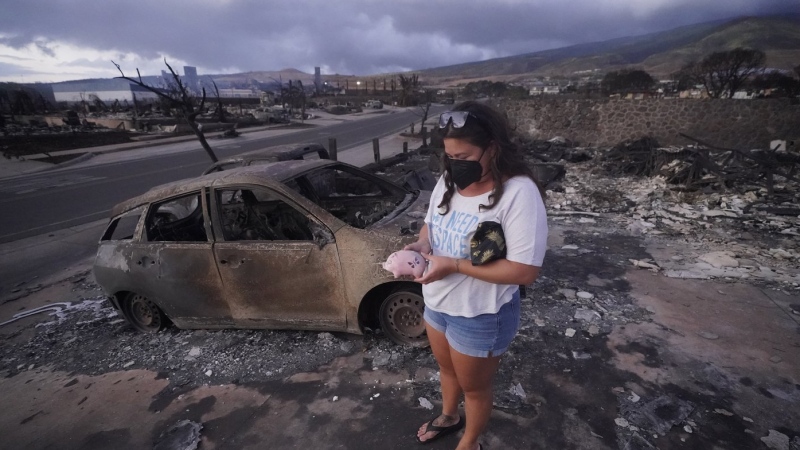 Summer Gerling picks up her piggy bank found in the rubble of her home following the wildfire on Aug. 10, 2023, in Lahaina, Hawaii. Lahaina residents are grappling with a range of feelings as Maui authorities plan to begin allowing them back into what has become known as the "burn zone." (AP Photo/Rick Bowmer, File)