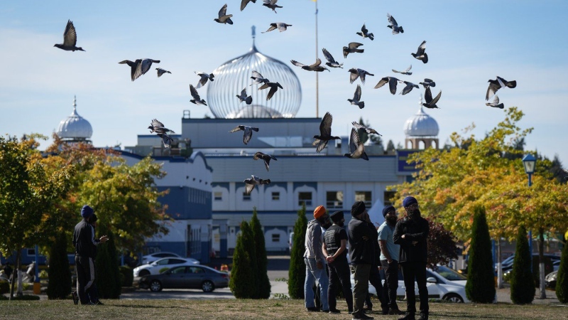 A flock of birds flies past as Moninder Singh, front right, a spokesperson for the British Columbia Gurdwaras Council (BCGC), waits to speak to reporters outside the Guru Nanak Sikh Gurdwara Sahib in Surrey, B.C., on Monday, September 18, 2023, where temple president Hardeep Singh Nijjar was gunned down in his vehicle while leaving the temple parking lot in June. THE CANADIAN PRESS/Darryl Dyck