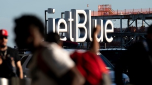 Travelers make their way near a JetBlue sign ahead of the Fourth of July holiday weekend at John F. Kennedy International Airport on June 28, 2022. in New York. Emergency responders evacuated a JetBlue flight at JFK International Airport in New York City as a result of a laptop emitting smoke on a plane Saturday evening, Dec. 24, officials said. (AP Photo/Julia Nikhinson, File)