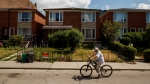 A person cycles by a row of houses in Toronto on July 12, 2022. (THE CANADIAN PRESS/Cole Burston)