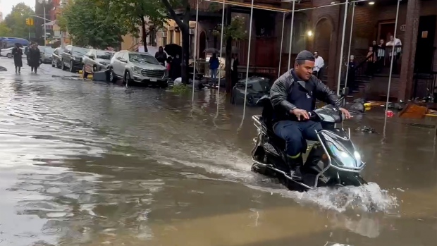 A State of Emergency has been declared in New York after a rainstorm swamped the metropolitan area, shutting down parts of the city's subway system, flooding streets and highways, and delaying flights. <br><br> In this photo taken from video, a man drives a scooter through flood waters, Friday, Sept. 29, 2023, in the Brooklyn borough of New York. (AP Photo/Jake Offenhartz) 