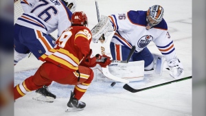 Edmonton Oilers goalie Jack Campbell, right, swats the puck away from Calgary Flames forward Dillon Dube during first period NHL pre-season hockey action in Calgary, Alta., Friday, Sept. 29, 2023. THE CANADIAN PRESS/Jeff McIntosh