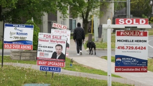 A person walks past multiple for-sale and sold real estate signs in Mississauga, Ont., on Wednesday, May 24, 2023. (THE CANADIAN PRESS/Nathan Denette)