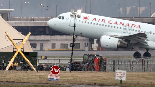 Members of the Canadian Forces, lower right, work outside temporary military service bays setup for CF-18 fighter jets involved in security for the Vancouver Winter Olympics as an Air Canada Airbus A320 takes off from Vancouver International Airport in Richmond, B.C., on Wednesday February 3, 2010. (Darryl Dyck/THE CANADIAN PRESS)