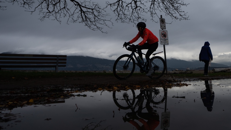 A person rides their bicycle in the rain at at Locarno Beach in Vancouver, B.C., Saturday, Nov. 11, 2023. THE CANADIAN PRESS/Ethan Cairns