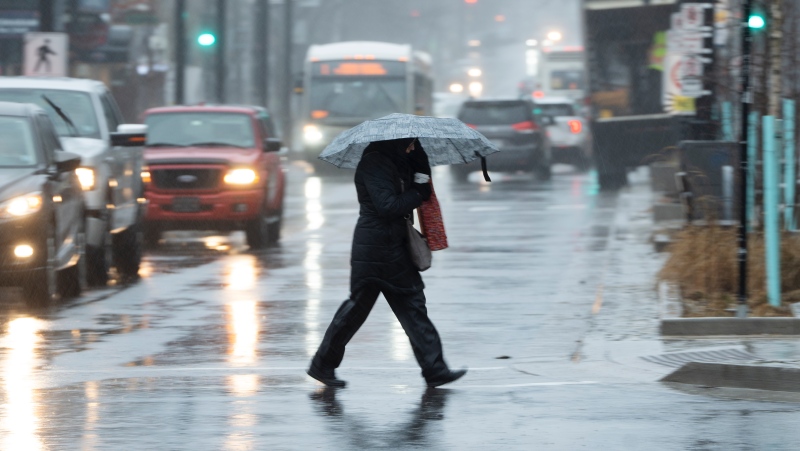 A pedestrians shield themselves from rain and wind during a rainfall warning in Halifax on Thursday, January 26, 2023. (THE CANADIAN PRESS/Darren Calabrese)
