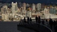 People are silhouetted on a walkway in downtown Vancouver, as condos and apartment buildings in North Vancouver are seen across the harbour, on Tuesday, Oct. 10, 2023. THE CANADIAN PRESS/Darryl Dyck