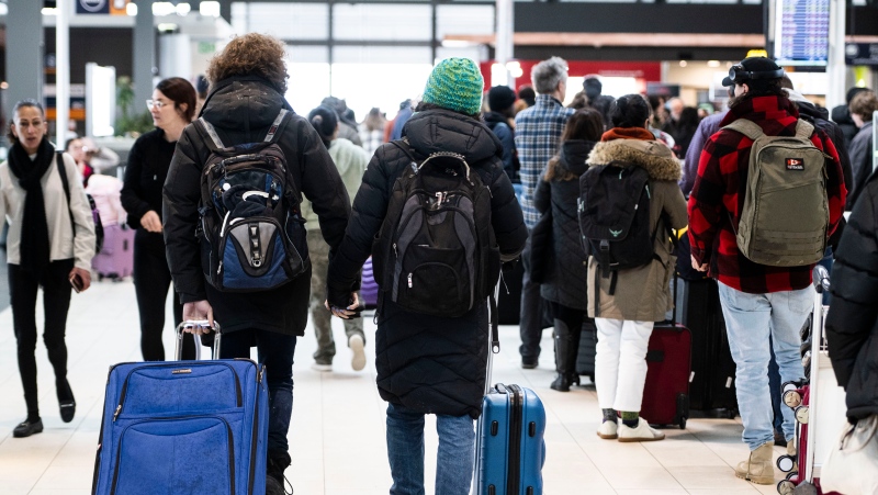 Travellers hold hands as they pass others lining up at the Ottawa International Airport on Friday, Dec. 23, 2022. THE CANADIAN PRESS/Justin Tang