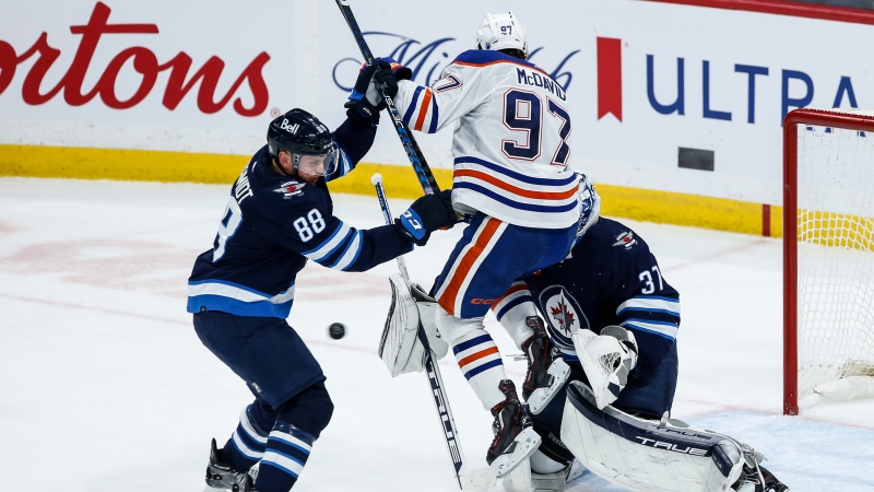 Edmonton Oilers' Connor McDavid (97) jumps in front of Winnipeg Jets goaltender Connor Hellebuyck (37) as Nate Schmidt (88) defends during third period NHL action in Winnipeg on Thursday, November 30, 2023. THE CANADIAN PRESS/John Woods
