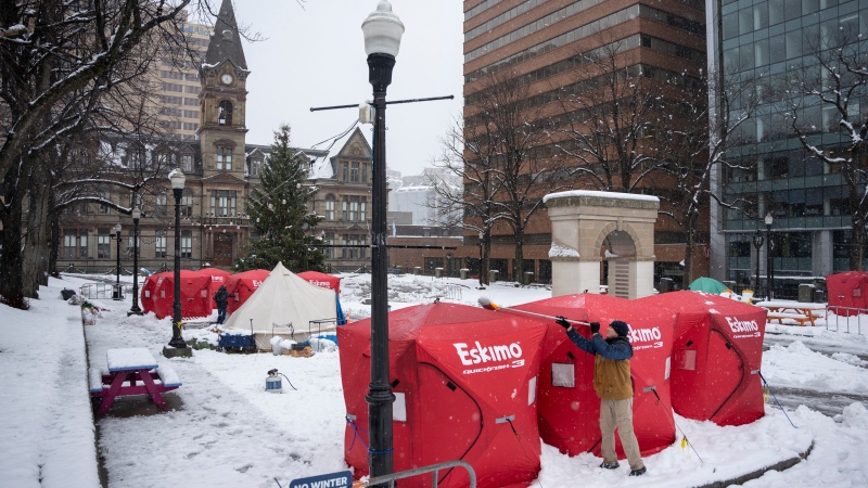 Matthew Grant uses a broom to clean snow off ice fishing enclosures at a tent encampment in front of City Hall in downtown Halifax, Monday, Dec. 4, 2023. THE CANADIAN PRESS/Darren Calabrese