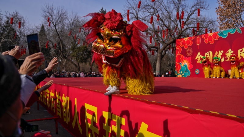 People gesture and film as artists perform an acrobatic lion dance on a stage at the Longtan Park's temple fair on the second day of Lunar New Year in Beijing, Sunday, Feb. 11, 2024. (AP Photo/Andy Wong)