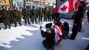 Protesters kneel in front of Surete du Quebec officers forming an enclosure around blockaded vehicles on Rideau Street, as police aim to end an ongoing protest against COVID-19 measures that has grown into a broader anti-government protest, on its 22nd day, in Ottawa, on Friday, Feb. 18, 2022. (Justin Tang/THE CANADIAN PRESS)