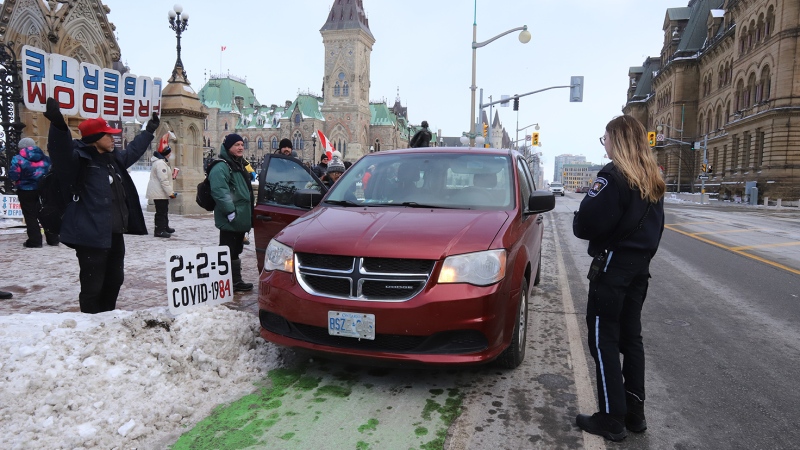A bylaw officer tells a motorist to move their vehicle as people attend the anniversary of the "Freedom Convoy" demonstrations on Parliament Hill in Ottawa on Saturday, Feb. 17, 2024. Thousands of demonstrators took over streets around Parliament Hill in late January 2022, blocking roads with big-rig trucks and other vehicles and refusing to move. (Patrick Doyle/THE CANADIAN PRESS)