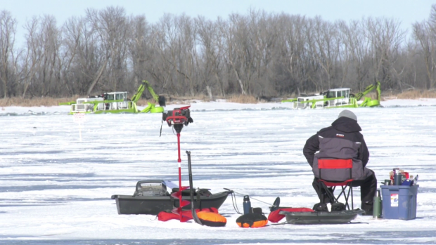 A man ice fishes on the Red River while ice cutters work in the distance on Feb. 20, 2024. (Image source: Danton Unger/ CTV News Winnipeg)