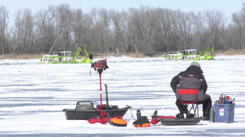 A man ice fishes on the Red River while ice cutters work in the distance on Feb. 20, 2024. (Image source: Danton Unger/ CTV News Winnipeg)