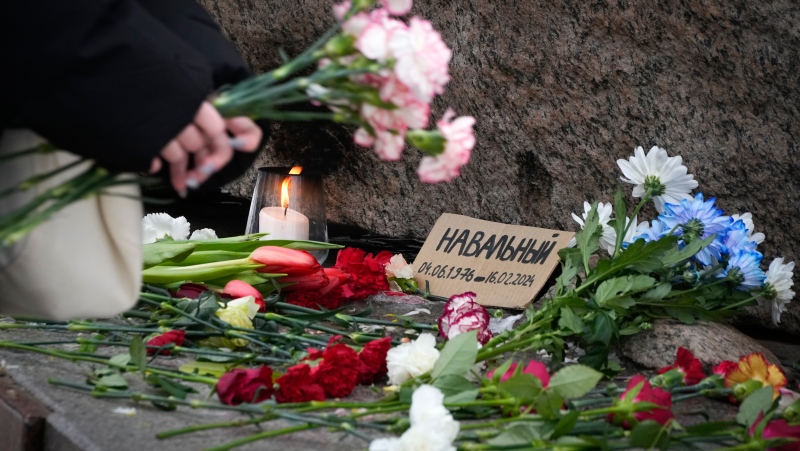 A woman pays tribute to Alexei Navalny at the monument, a large boulder from the Solovetsky islands, where the first camp of the Gulag political prison system was established in St. Petersburg, Russia, on Wednesday, Feb. 21, 2024. (AP Photo/Dmitri Lovetsky)