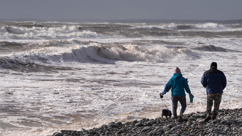 Hikers walk along Lawrencetown Beach Provincial Park in , Lawrencetown, N.S. as waves and heavy winds battered the coastline on Sunday, January 14, 2024. (Source: THE CANADIAN PRESS/Darren Calabrese)