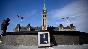 A person stands by the Centennial Flame near a framed portrait of former prime minister Brian Mulroney that was left there, as Canadians mourn his death at the age of 84, in Ottawa, on Friday, March 1, 2024. THE CANADIAN PRESS/Justin Tang